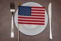 The American flag lies on a plate between a knife and a fork