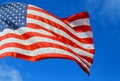 American flag red, white and blue with stars and strips in the wind blue sky