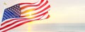 american flag waving in the wind at sunrise, against the background of the ocean, 3d image, wide format with copy space Royalty Free Stock Photo