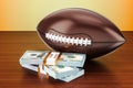 American football ball with dollar packs on the wooden table, 3D rendering