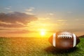 American football ball on green grass field on background of sunset sky. Banner. Royalty Free Stock Photo