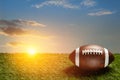 American football ball on green grass field on background of sunset sky. Banner. Royalty Free Stock Photo