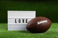 American football ball and lightbox with word Love on green grass Royalty Free Stock Photo