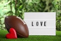 American football ball, lightbox with word Love and heart on green grass against blurred background Royalty Free Stock Photo