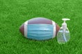 An American Football with a face mask and hand sanitizer on the right on field with green grass. Concept Football during pandemic Royalty Free Stock Photo