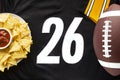 An American football with organic nacho chips and mild salsa on a white black football jersey with the 26 number on horizontal