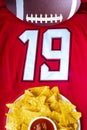 An American football with organic nacho chips and mild salsa on a white red football jersey with the 19 number