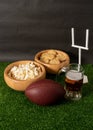 American football ball, beer, snacks and goal post on green grass and black background Royalty Free Stock Photo