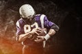 American football player holding ball in his hands in smoke. Black background, copy space. The concept of American