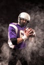 American football player holding ball in his hands in smoke. Black background, copy space. The concept of American Royalty Free Stock Photo