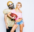 American football player in uniform and helmet posing with beautiful long-legged blond girl cheerleader dressed in a T