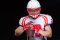 American football player wearing helmet posing with ball on black background Royalty Free Stock Photo