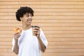 American guy holding a cup of coffee and an orange glazed donut, looking away and wearing a white T-shirt Royalty Free Stock Photo