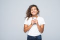 American latin woman with curly hair holding mobile phone and smiling on camera isolated over white background Royalty Free Stock Photo