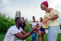 American male standing on one knee asking woman marriage giving ring proposing surprised shocked while gathering group Royalty Free Stock Photo