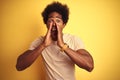 American man with afro hair wearing striped t-shirt standing over isolated yellow background Shouting angry out loud with hands Royalty Free Stock Photo