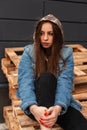 American modern pretty stylish young woman in youth fashionable denim clothes with a military hood posing on wooden pallets