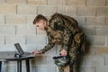 American soldier in military uniform using laptop computer for drone controlling and to stay in contact with friends and Royalty Free Stock Photo