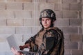 American soldier in military uniform using laptop computer for drone controlling and to stay in contact with friends and Royalty Free Stock Photo