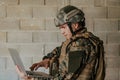 American soldier in military uniform using laptop computer for drone controlling and to stay in contact with friends and Royalty Free Stock Photo