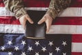 American soldier mourning and praying with the Bible in his hands and the American flag