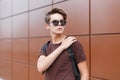 American stylish hipster young man in a brown stylish t-shirt in dark sunglasses with a trendy hairstyle with Royalty Free Stock Photo