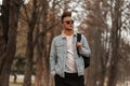 American stylish young man hipster with a trendy hairstyle in fashionable clothes with a black backpack in trendy sunglasses Royalty Free Stock Photo