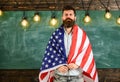 American teacher covered with american flag. Man with beard and mustache on serious face with flag of USA, chalkboard on Royalty Free Stock Photo