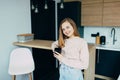 American teenage girl at Home kitchen interior holding Black coffee cup. Woman in pink blouse and blue jeans lean on wooden counte Royalty Free Stock Photo