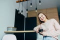 American teenage girl at Home kitchen interior holding Black coffee cup. Woman in pink blouse and blue jeans lean on wooden counte Royalty Free Stock Photo