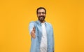 Amiable man in a denim shirt reaching out for a handshake, smiling warmly