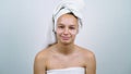 Amiable teenager wrapped in bath towels smiling at camera in white studio