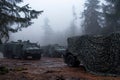 Military vehicles concealed under camo netting in misty forest environment. Generative AI