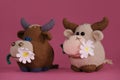 Amigurumi cow dolls on pink background. A soft DIY toy made of cotton and natural wool. Two brown bulls with a daisy in