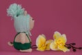 Amigurumi kitten doll on pink background next to yellow orchid flowers. A soft DIY toy made of cotton. One brown cat
