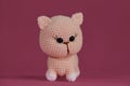 Cute little crocheted cat, handmade art. Amigurumi kitten doll on pink background. A soft DIY toy made of natural cotton