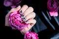 AMOR word on nails manicure hold Pink rose flower on black silk fabric. Minimal flat lay nature. Female hand. Love Royalty Free Stock Photo