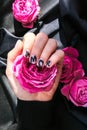 AMOR word on nails manicure hold Pink rose flower on black silk fabric. Minimal flat lay nature. Female hand. Love Royalty Free Stock Photo