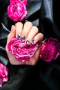 AMOR word on nails manicure hold Pink rose flower on black silk fabric. Minimal flat lay nature. Female hand. Love Royalty Free Stock Photo