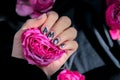 AMOR word on nails manicure hold Pink rose flower on black silk fabric. Minimal flat lay nature. Female hand. Love Royalty Free Stock Photo