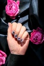 AMOR word on nails manicure hold Pink rose flower on black silk fabric. Minimal flat lay nature. Female hand. Love Royalty Free Stock Photo