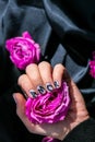 AMOR word on nails manicure hold Pink rose flower on black silk fabric. Minimal flat lay nature. Female hand. Love Royalty Free Stock Photo