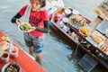 Amphawa, Thailand: a girl serves a plate with squid rings, standing in the water with her boat behind at Amphawa Floating Market