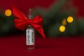 Ampoule of the COVID-19 coronavirus vaccine stands as a gift near Christmas tree branch with lights on a red background