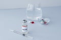 Ampoule with vaccine, syringe in foreground and different pills and glass water on background. Royalty Free Stock Photo