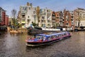 AMSTERDAM, NETHERLANDS - APRIL 10, 2018: Amsterdam canal with typical dutch houses and touristic boat on foreground, Amsterdam, Ne