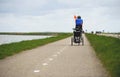 AMSTERDAM, NETHERLANDS, April 2017: Man on the Bike Pulling Baby Cart for a Bicycle Chariot by Thule. Bicycle path with Lake on