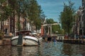 Kayak paddler on tree-lined canal with boat, buildings and blue sky in Amsterdam.