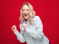 Amused beautiful young woman with closed eyes and clenched fists, isolated on red background. Yes concept. Amusing girl celebrates