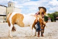 Amused cowboy girl having fun with pony outside stable Royalty Free Stock Photo